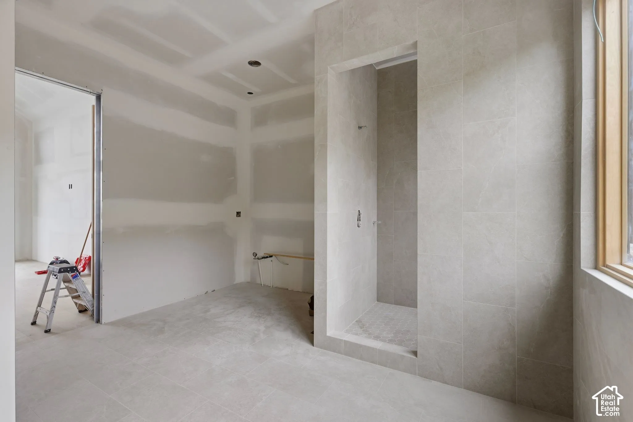 Walk-in shower enclosure featuring floor-to-ceiling neutral tile surrounds, recessed lighting, and natural light via a wood-trimmed window
