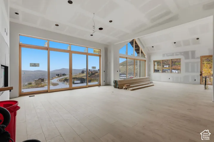 Open-concept interior featuring vaulted ceilings, floor-to-ceiling windows, wood-finish flooring, and a stone-clad fireplace