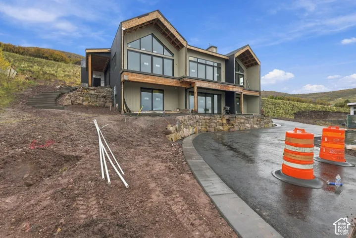 Modern multi-gabled exterior featuring dark metal siding, wood-trimmed rooflines, floor-to-ceiling windows, and integrated natural stone retaining walls