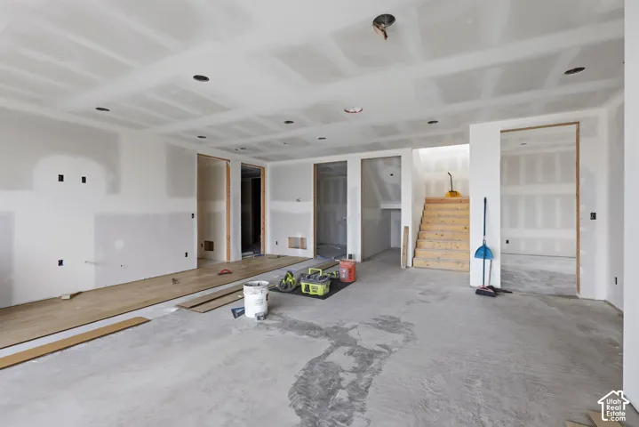Open-concept interior featuring recessed lighting, unfinished drywall, wood-finish flooring, and a wooden staircase