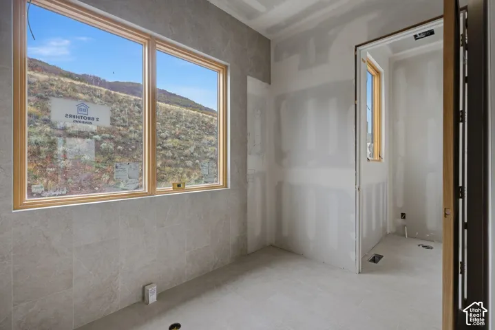 Interior space featuring large windows with natural-finish frames, neutral-toned tiled wall surfaces, and hillside scenery