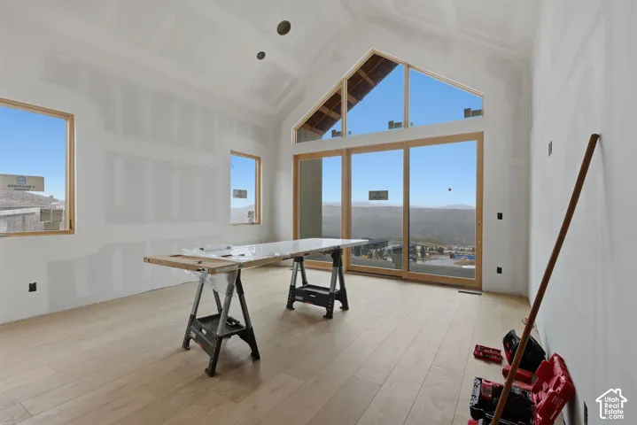 Vaulted ceiling with gable-style windows, expansive wood-frame glass doors, and light-toned wood-finish flooring