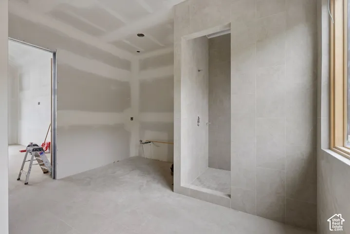 Walk-in shower enclosure featuring floor-to-ceiling neutral tile surrounds, recessed lighting, and natural light via a wood-trimmed window