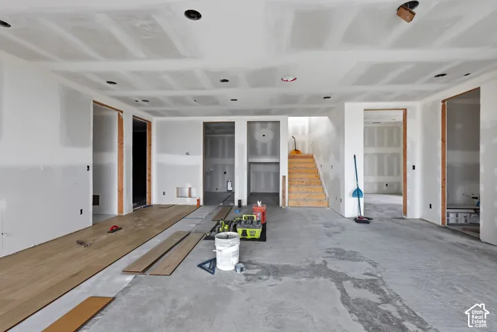 Unfinished interior space featuring drywall, recessed lighting, wood-finish flooring in progress, and an exposed wooden staircase