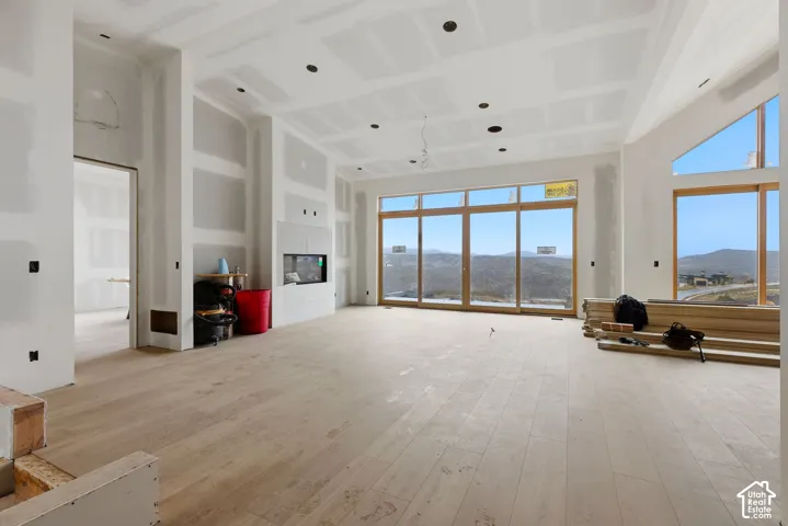 Open-concept interior featuring light-toned wood-finish flooring, floor-to-ceiling glass panel windows, a built-in linear fireplace, recessed lighting, and vaulted ceilings