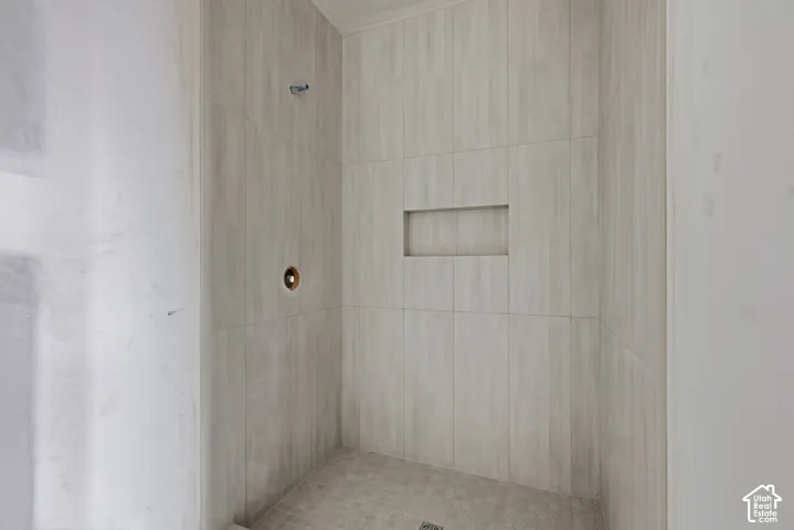 Walk-in shower featuring floor-to-ceiling light-toned tile, integrated wall niche, and pebble-finish shower floor