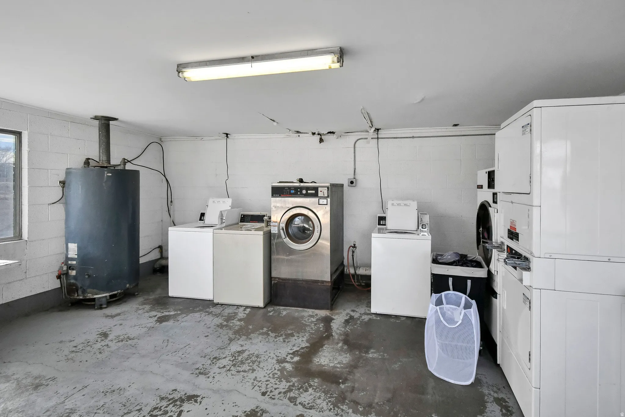 Shared laundry featuring concrete block wall, unfinished concrete flooring, water heater, and washer and clothes dryer