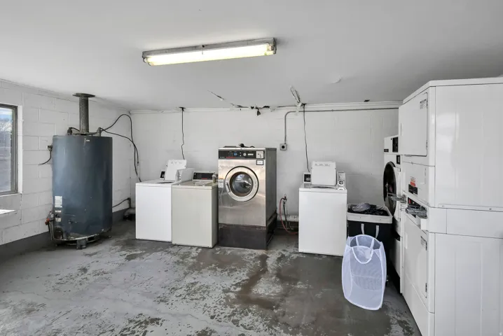 Shared laundry featuring concrete block wall, unfinished concrete flooring, water heater, and washer and clothes dryer