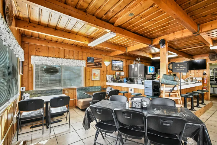 Dining room with light tile patterned floors, a wood ceiling with exposed beams, and wood walls