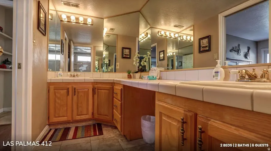 Full bathroom with double vanity, a textured ceiling, and dark tile patterned flooring