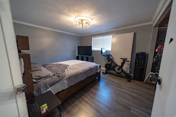 Bedroom featuring a textured ceiling, a closet, wood finished floors, and crown molding