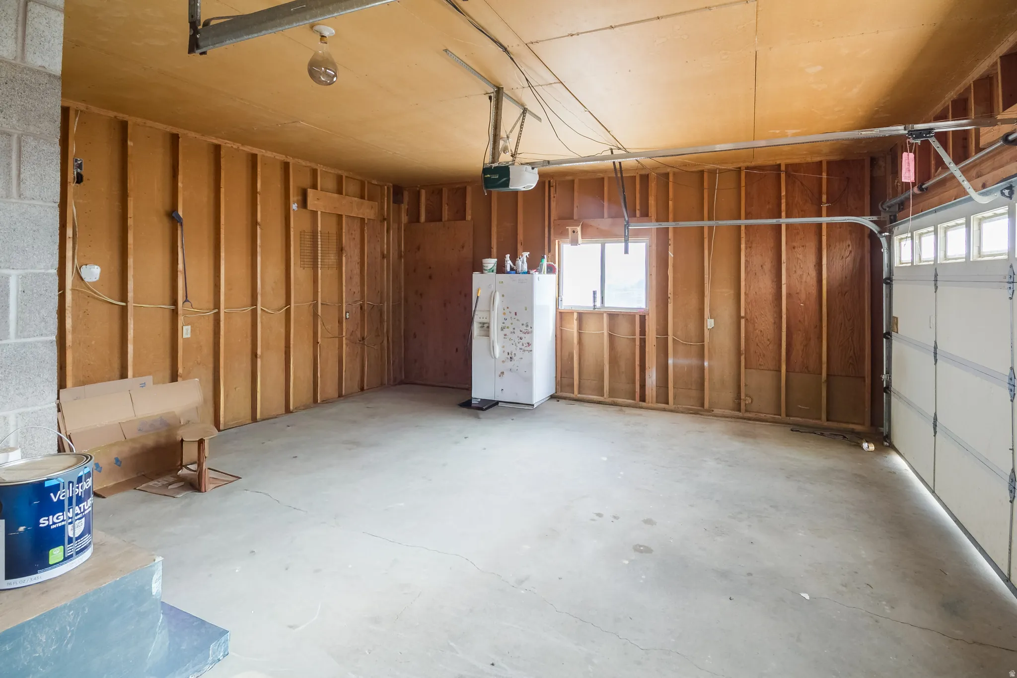Garage with white refrigerator with ice dispenser and a garage door opener