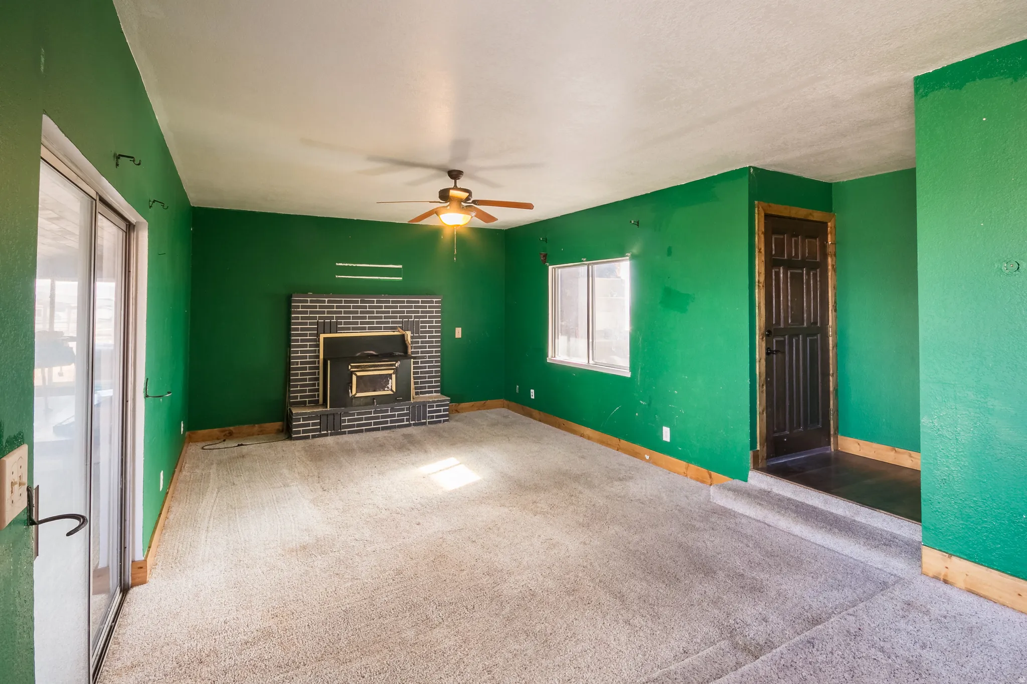 Unfurnished living room with ceiling fan, carpet flooring, and a brick fireplace