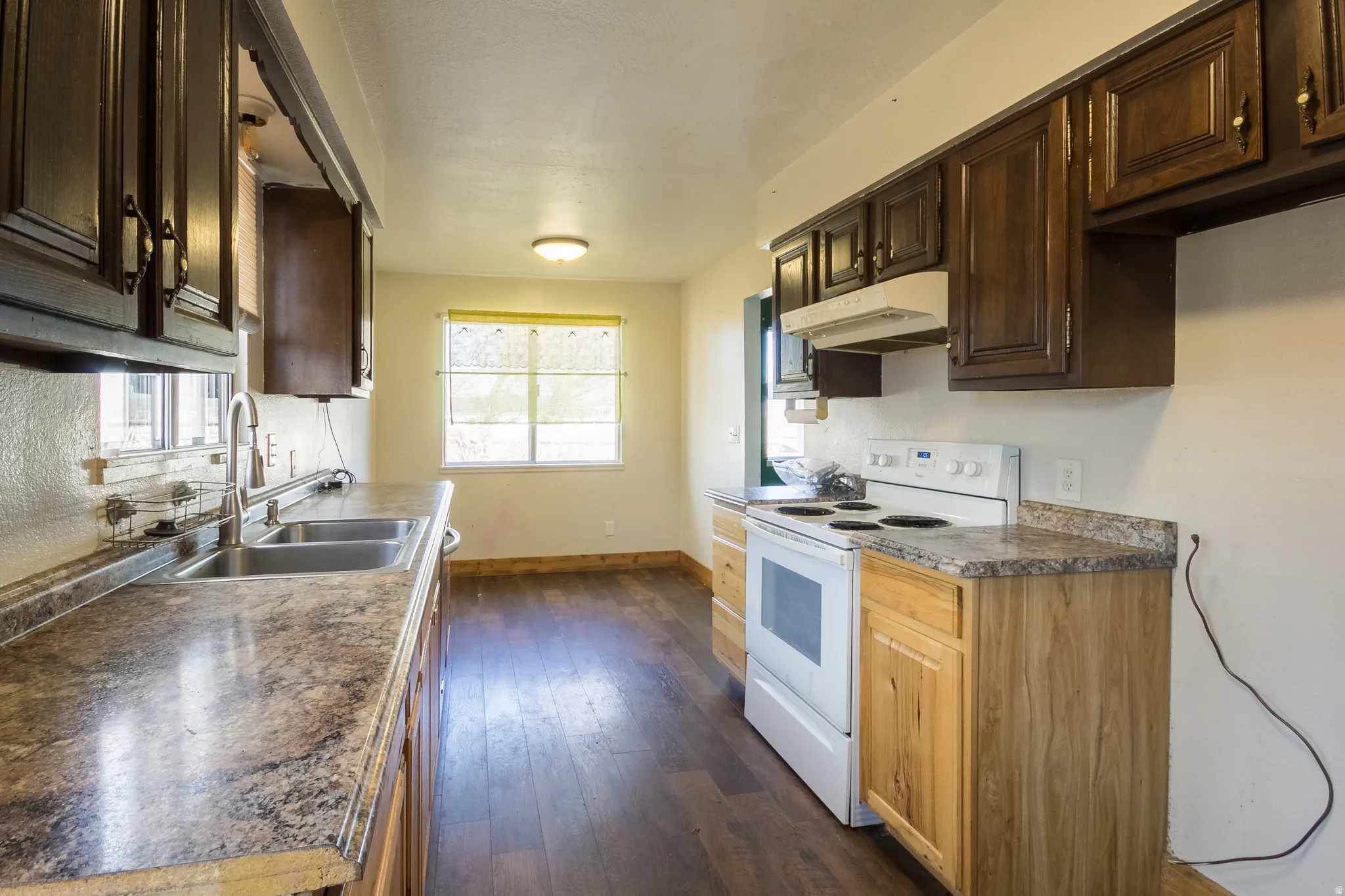 Kitchen featuring white range with electric stovetop, under cabinet range hood, dark wood-style floors, dark countertops, and dark brown cabinetry