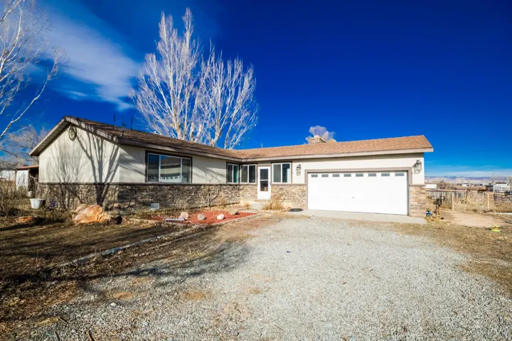 Single story home with gravel driveway, a garage, stone siding, and stucco siding