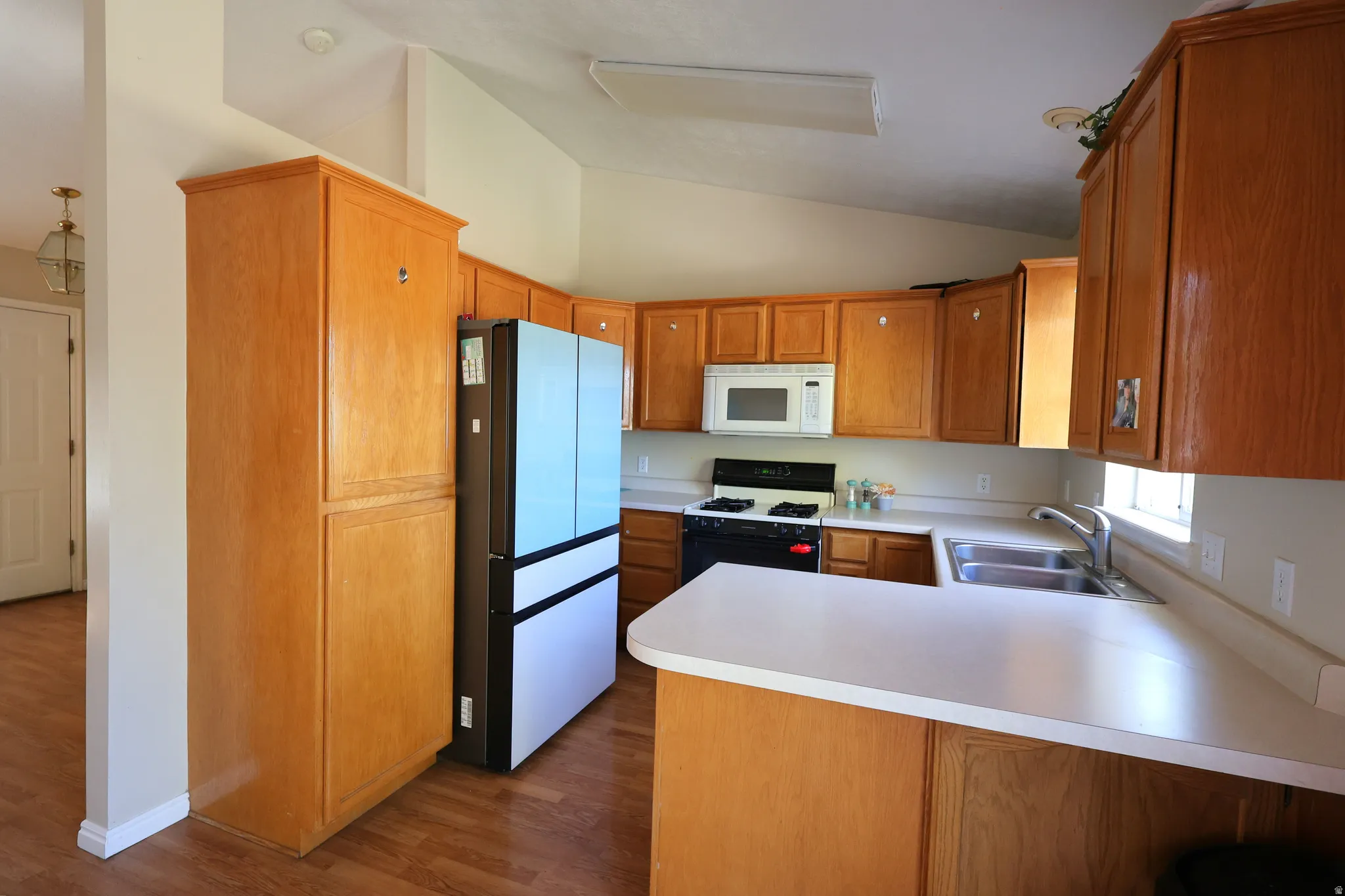 Kitchen featuring freestanding refrigerator, range with gas cooktop, vaulted ceiling, a peninsula, and dark wood-type flooring