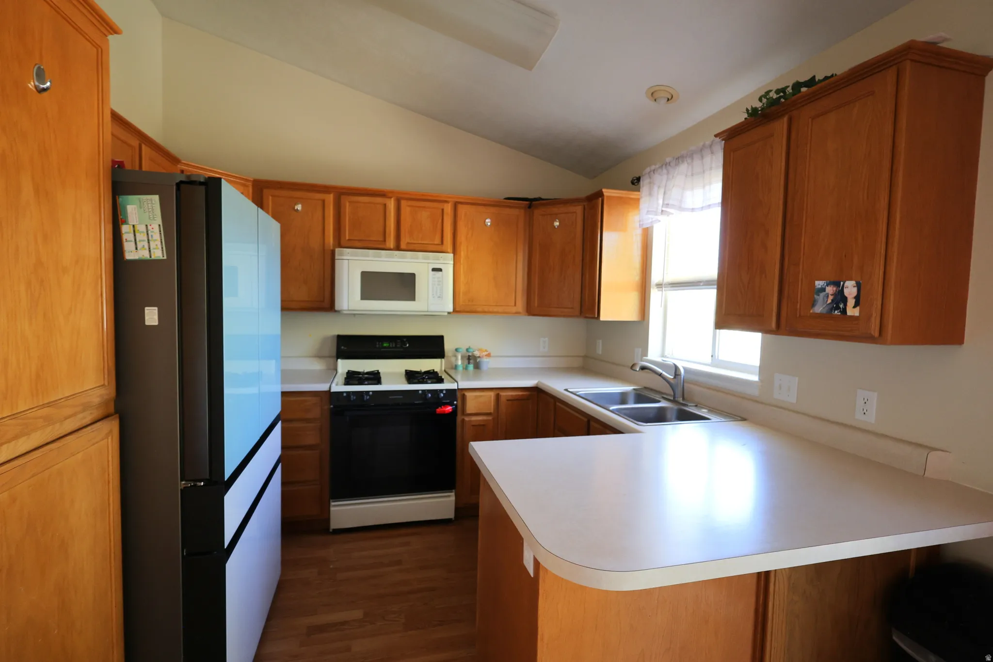 Kitchen featuring a peninsula, range with gas cooktop, freestanding refrigerator, brown cabinetry, and light countertops