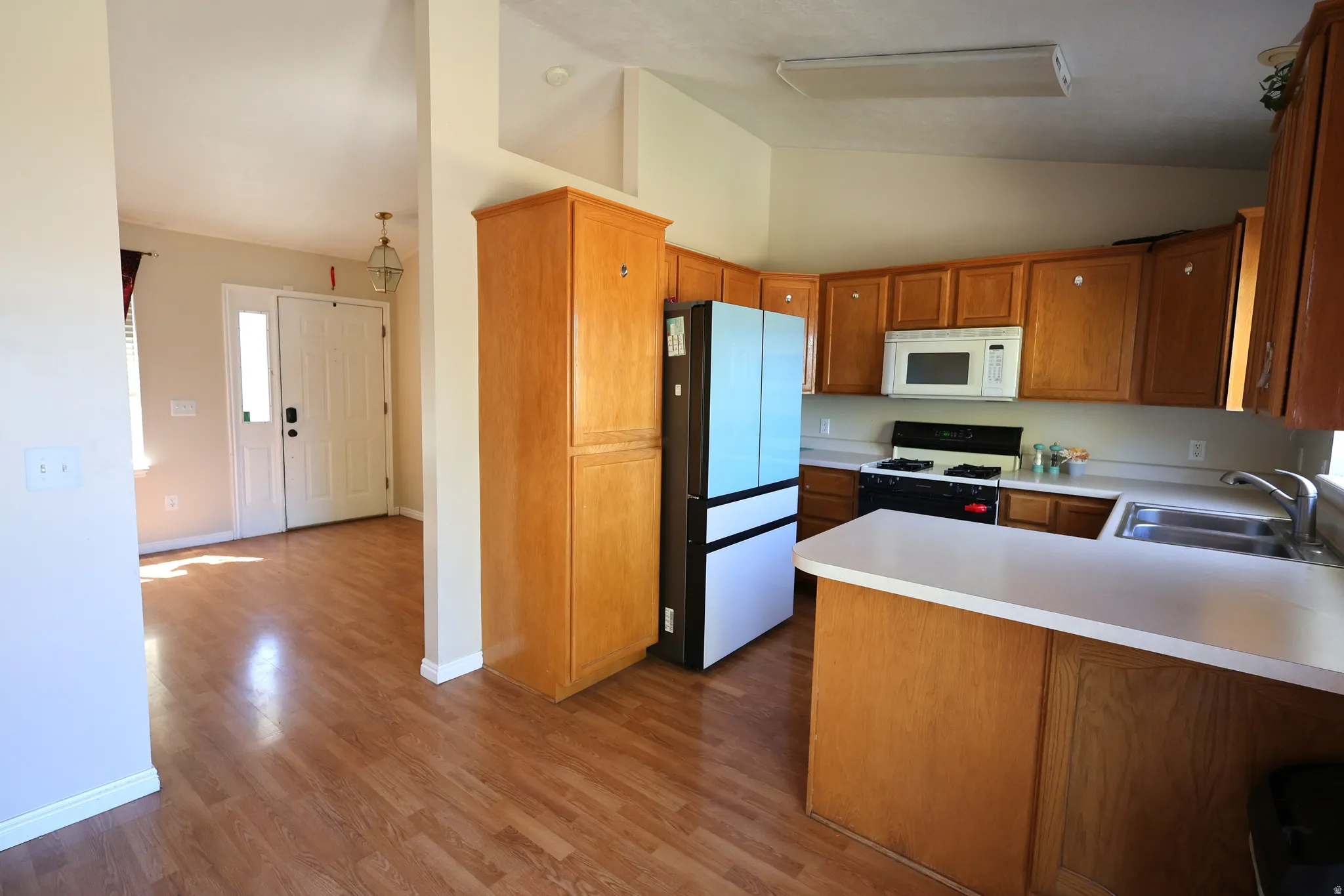 Kitchen with light countertops, brown cabinets, gas range oven, lofted ceiling, and freestanding refrigerator
