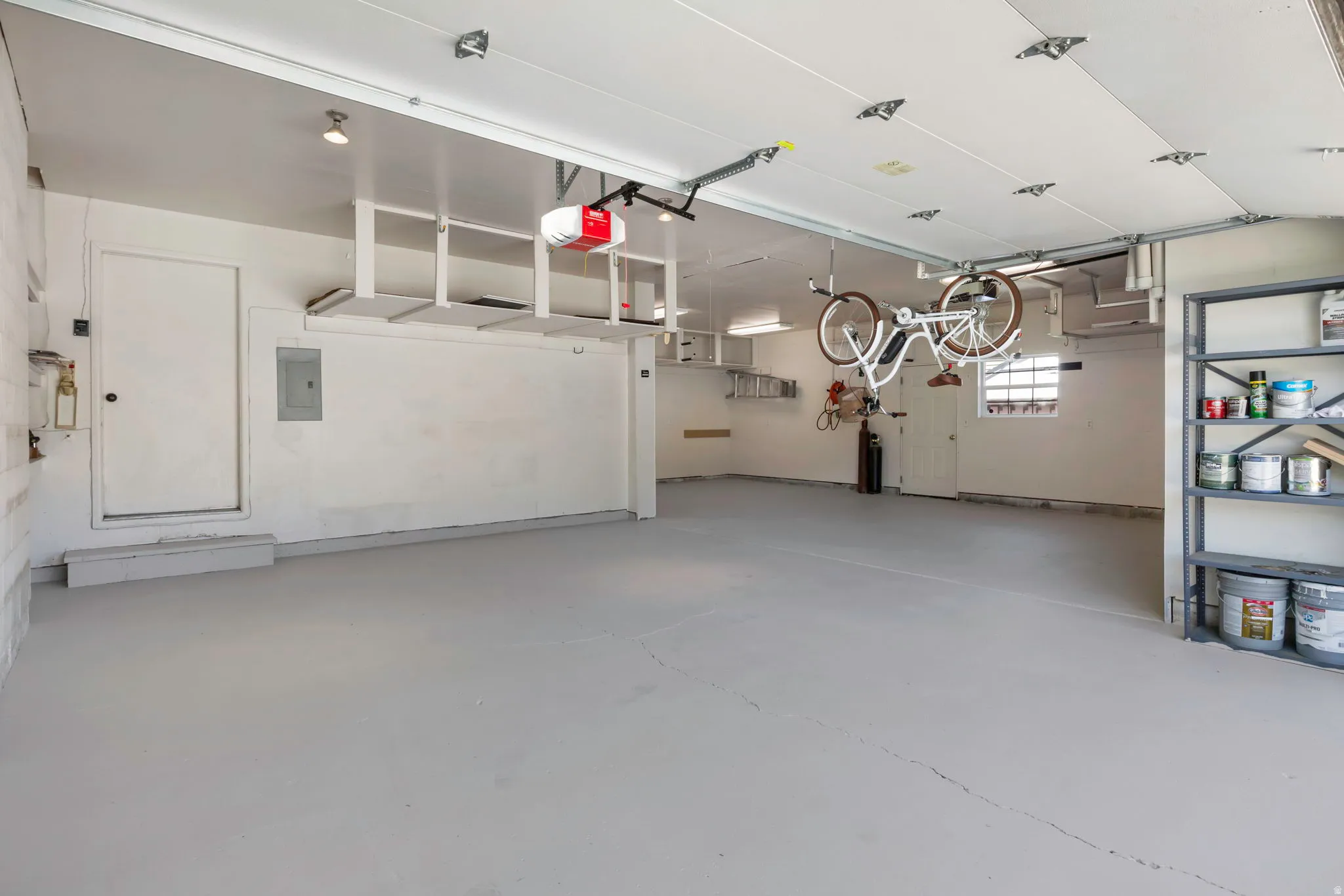 Spacious garage featuring a light gray floor, white painted walls, overhead storage racks, and a garage door opener system