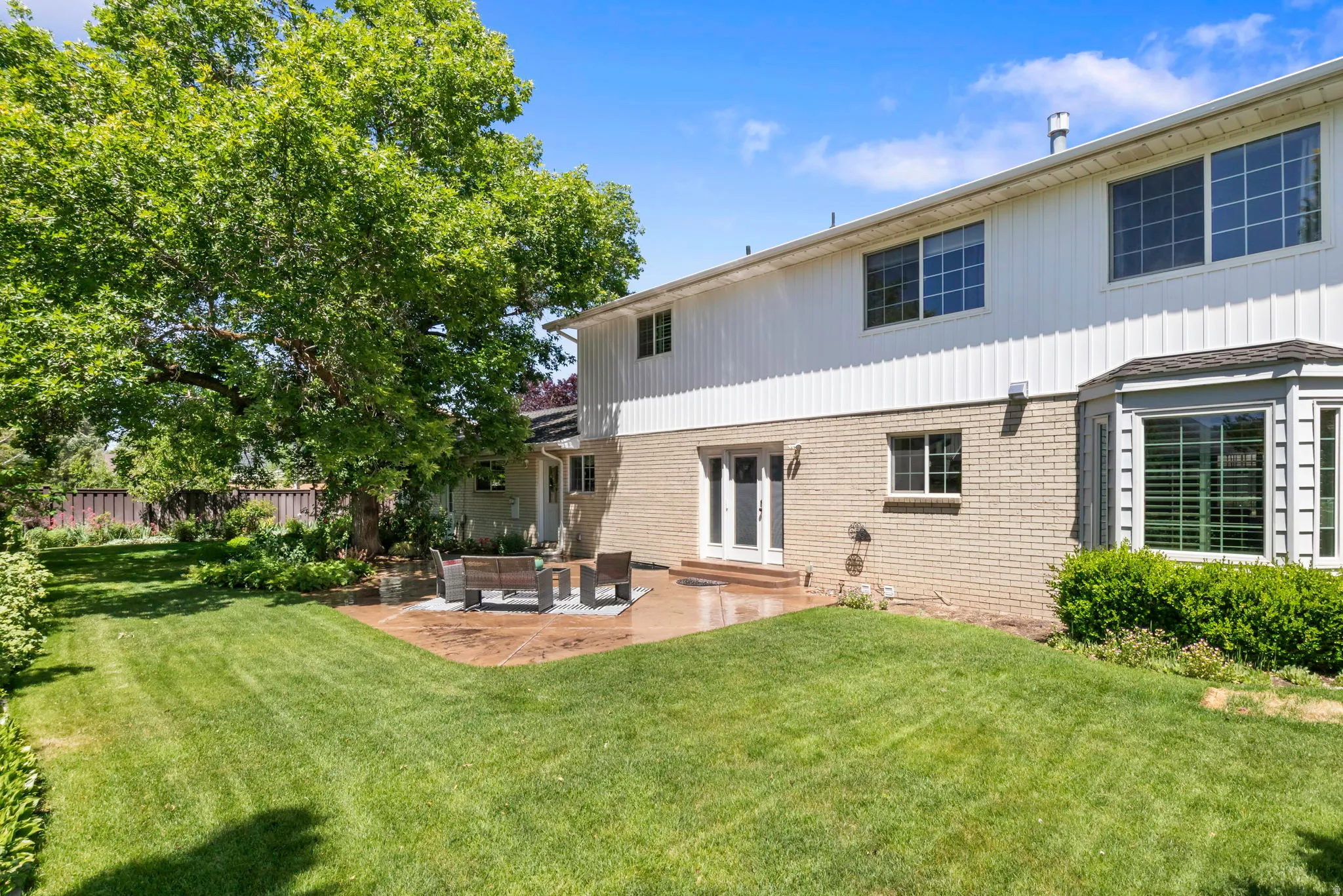 Expansive backyard featuring a large green lawn, mature tree, and a concrete patio