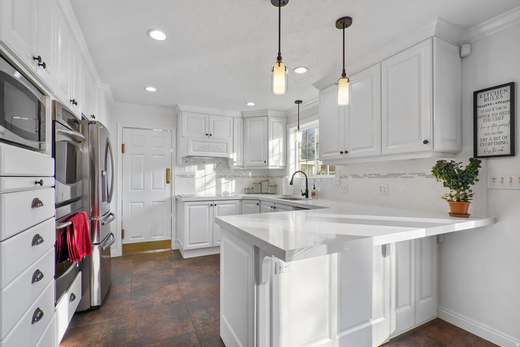 Kitchen featuring white cabinets, new quartz countertops, hanging light fixtures, crown molding, a peninsula, and stainless steel appliances