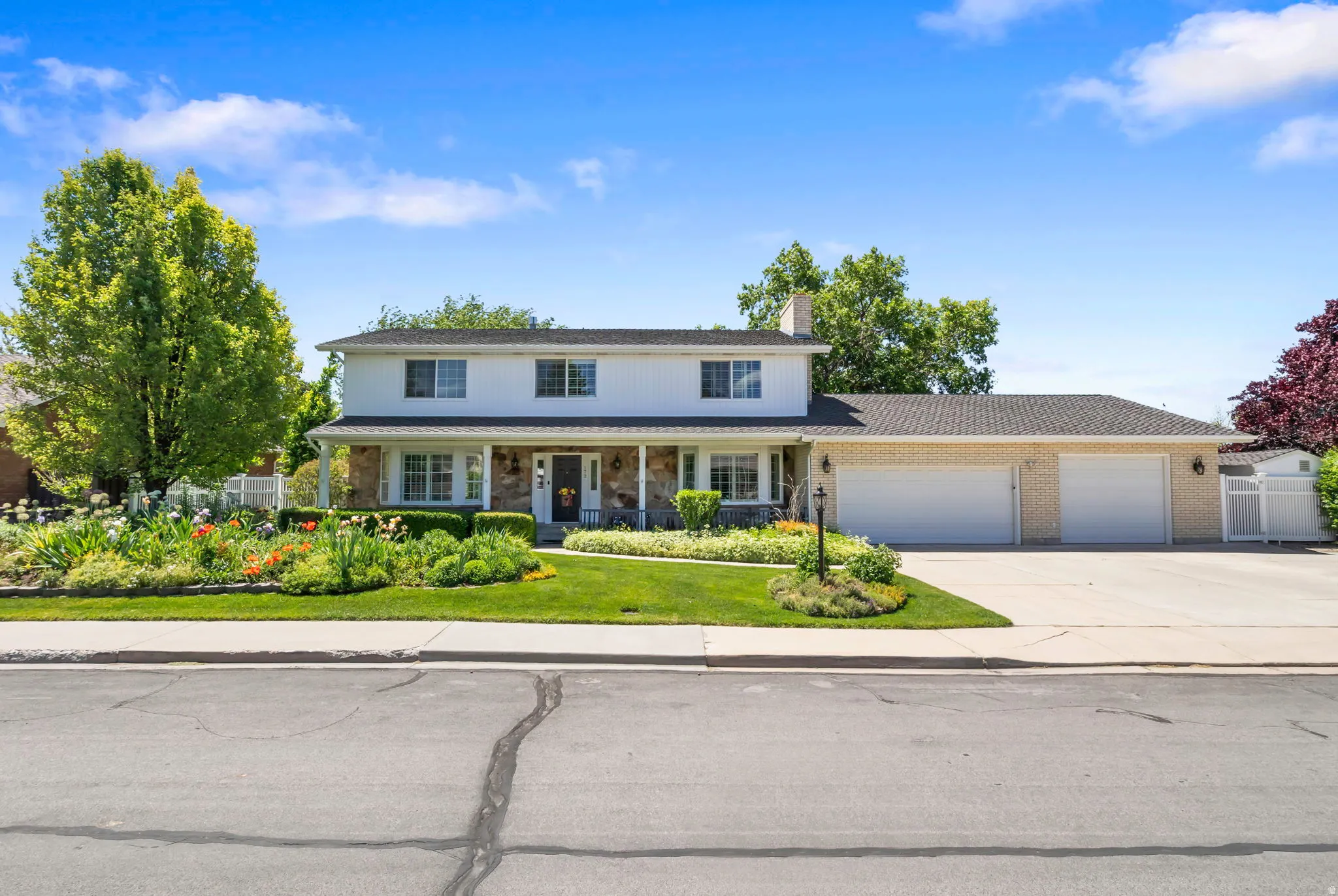 Two-story residence featuring a white facade with stone accents, a covered front porch, and a three-car garage