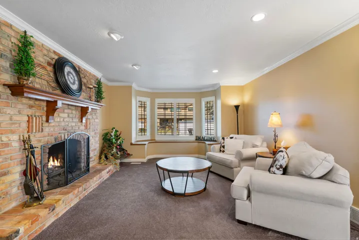 Family room with bay windows, storage bench, plantation shutters, crown molding, a brick fireplace, carpet, and recessed lighting