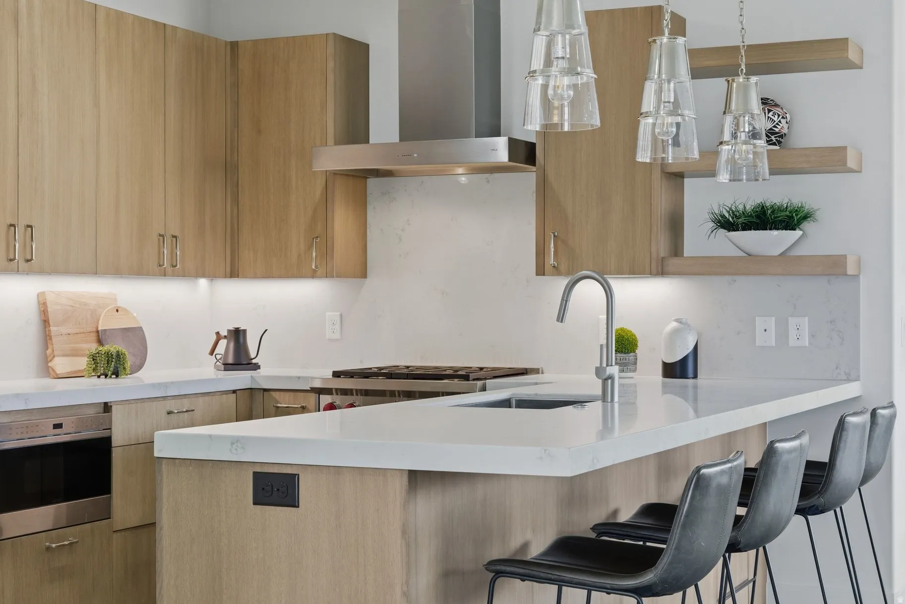 Kitchen featuring wall chimney exhaust hood, modern cabinets, light stone countertops, and pendant lighting