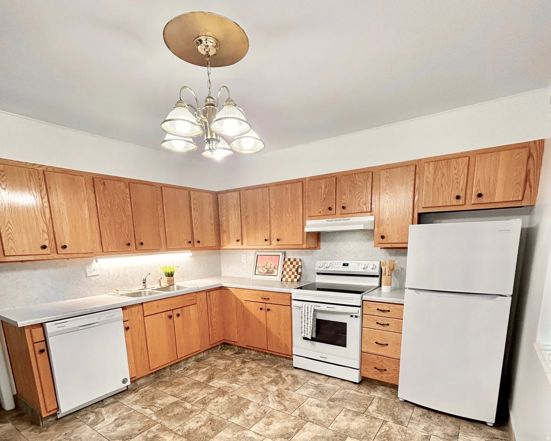 Kitchen featuring ample wood cabinetry, white appliances, L-shaped countertop, under-cabinet lighting, and patterned flooring