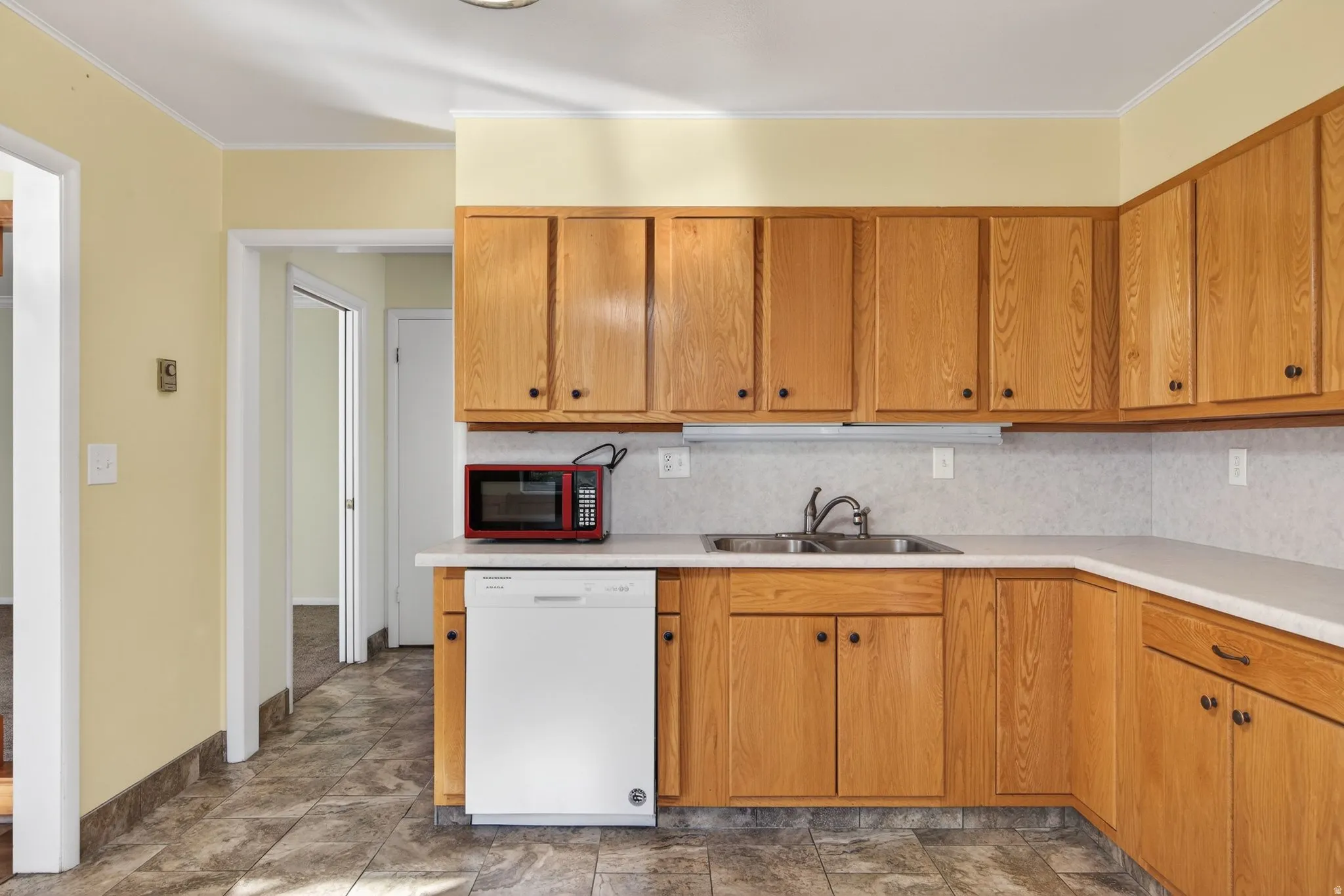 Kitchen featuring dishwasher, light countertops, backsplash, brown cabinetry, and ornamental molding