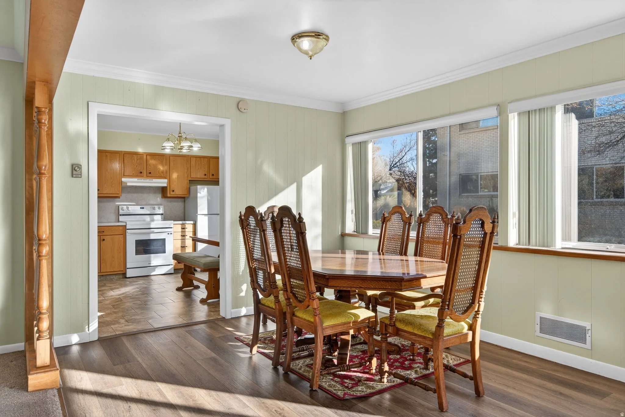 Dining area featuring plenty of natural light, dark wood-style LVP floors, ornamental molding, and a chandelier