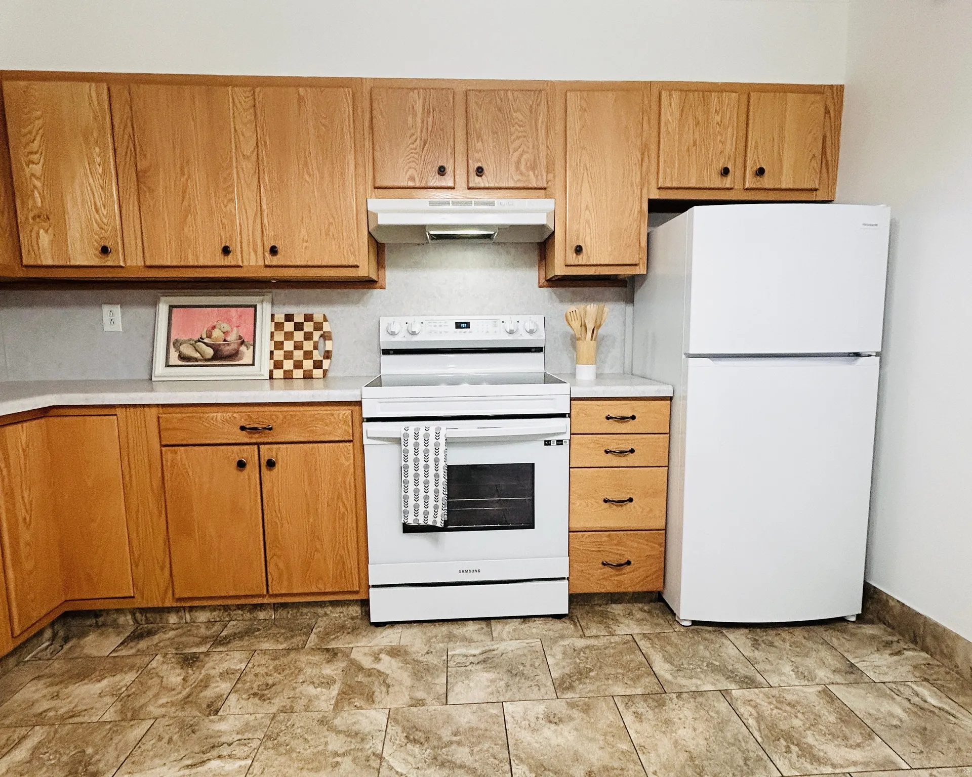 Kitchen featuring wood cabinetry, white appliances, light countertops, a white range with overhead vent, and neutral-toned tile flooring