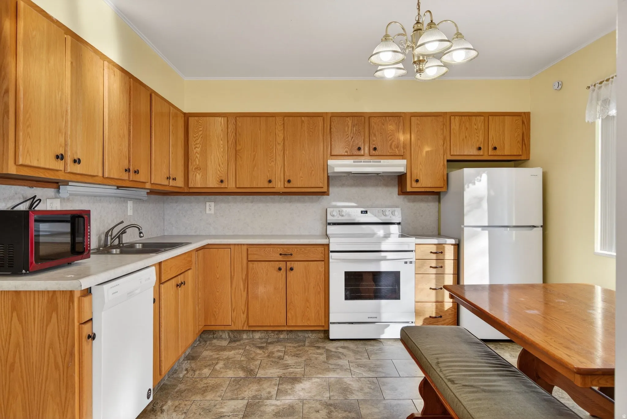 Kitchen with white appliances, backsplash, light countertops, pendant lighting, and stone finish floors