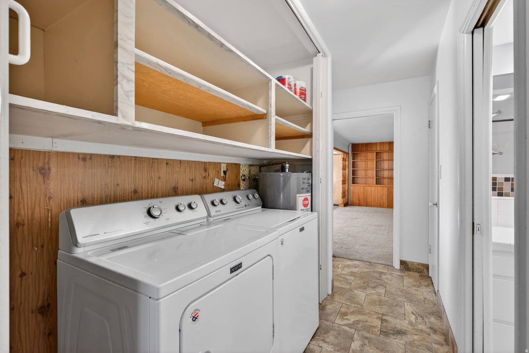 Laundry area with washing machine and clothes dryer, stone finish floors, and water heater