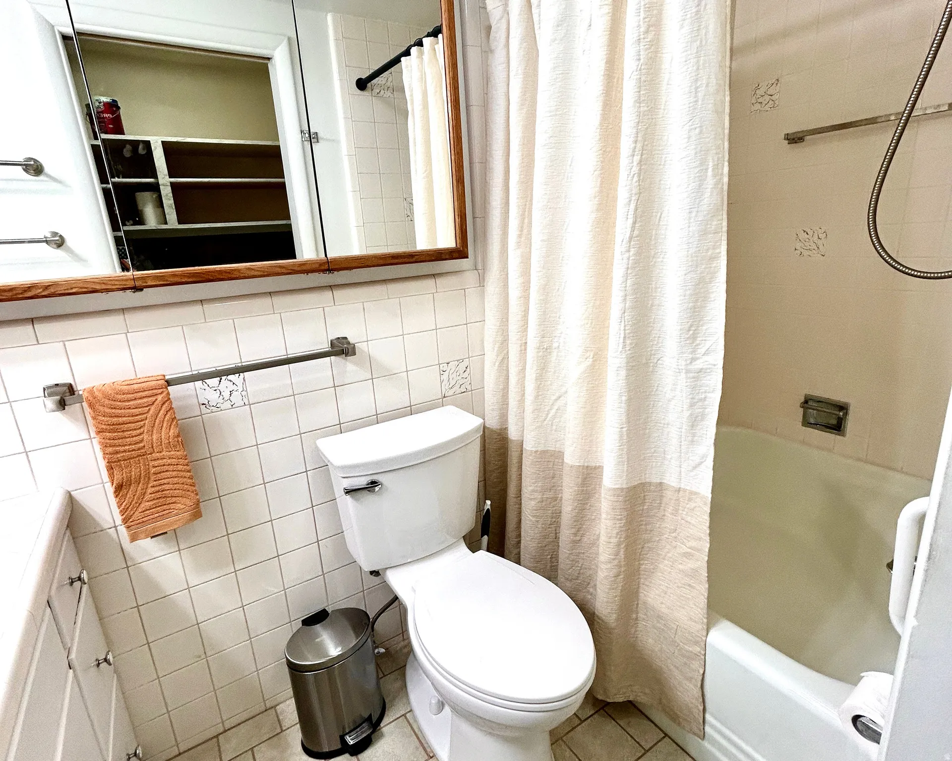 Bathroom featuring a white toilet, white square tile walls, and a built-in bathtub with shower curtain