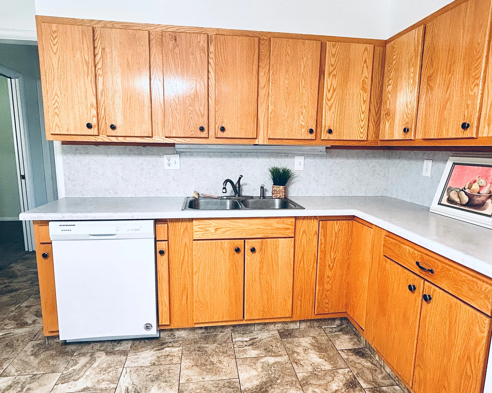 Kitchen featuring wood-finish cabinetry, a double basin sink, white countertops, and a white dishwasher