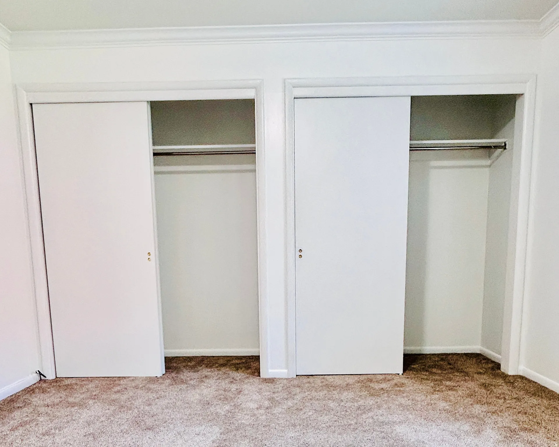 Dual sliding door closets featuring chrome hanging rods, white trim, and crown molding