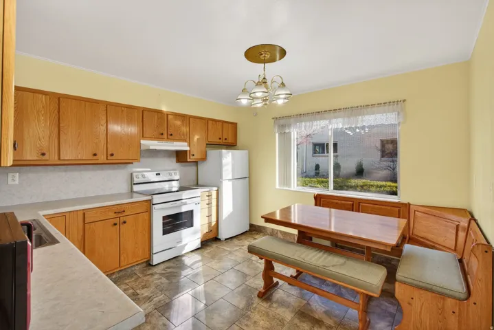 Kitchen with white appliances, light countertops, pendant lighting, backsplash, and brown cabinets