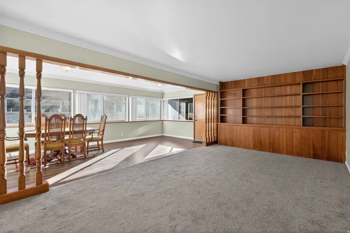 Carpeted living area featuring built in shelves and ornamental molding