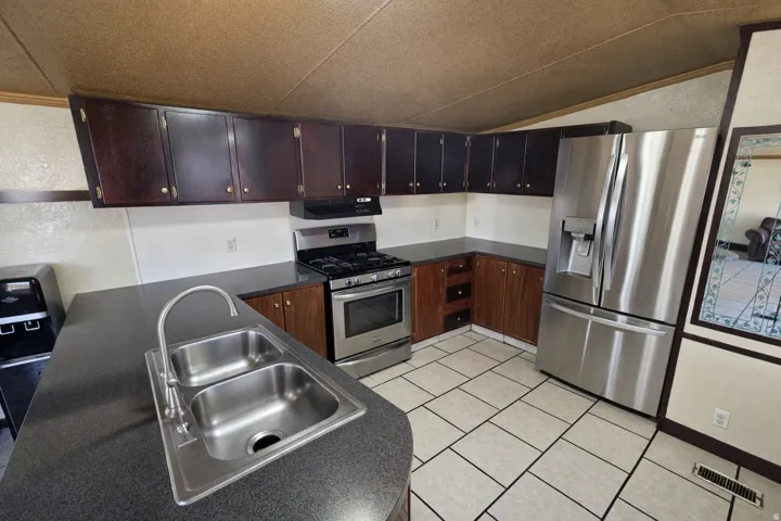 Kitchen with dark countertops, stainless steel appliances, dark wood finish cabinets, extractor fan, and light tile patterned floors