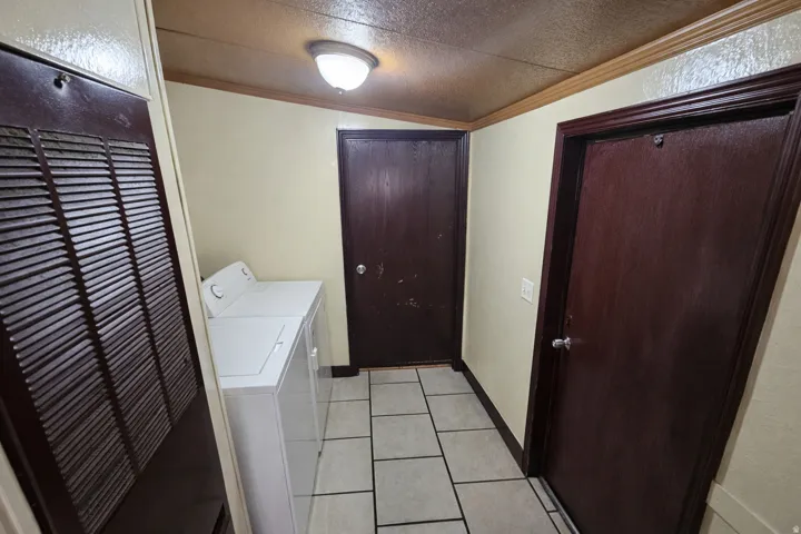 Laundry room featuring a heating unit, crown molding, light tile patterned flooring, and washer and clothes dryer