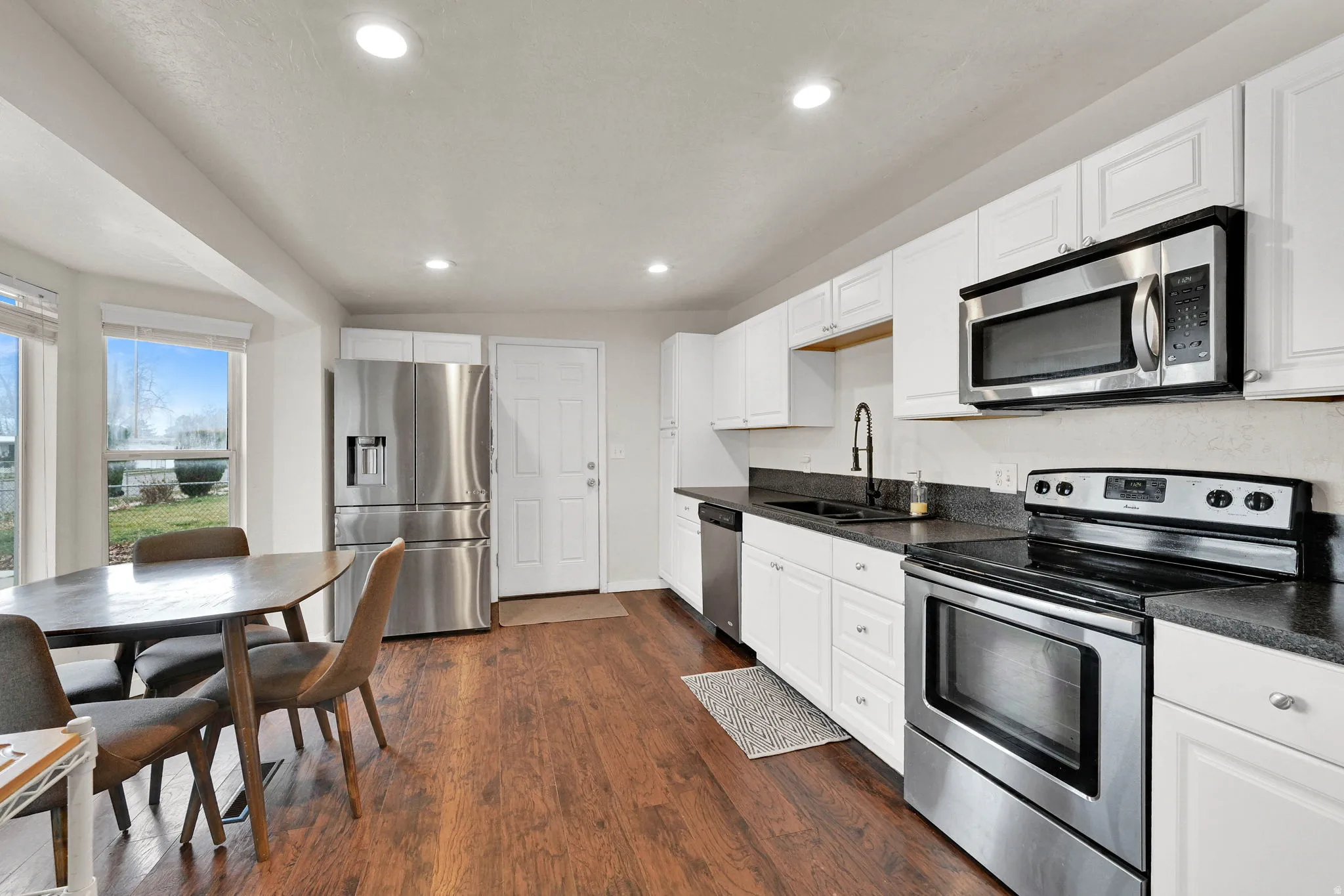 Kitchen with stainless steel appliances, white cabinets, dark countertops, dark wood finished floors, and recessed lighting