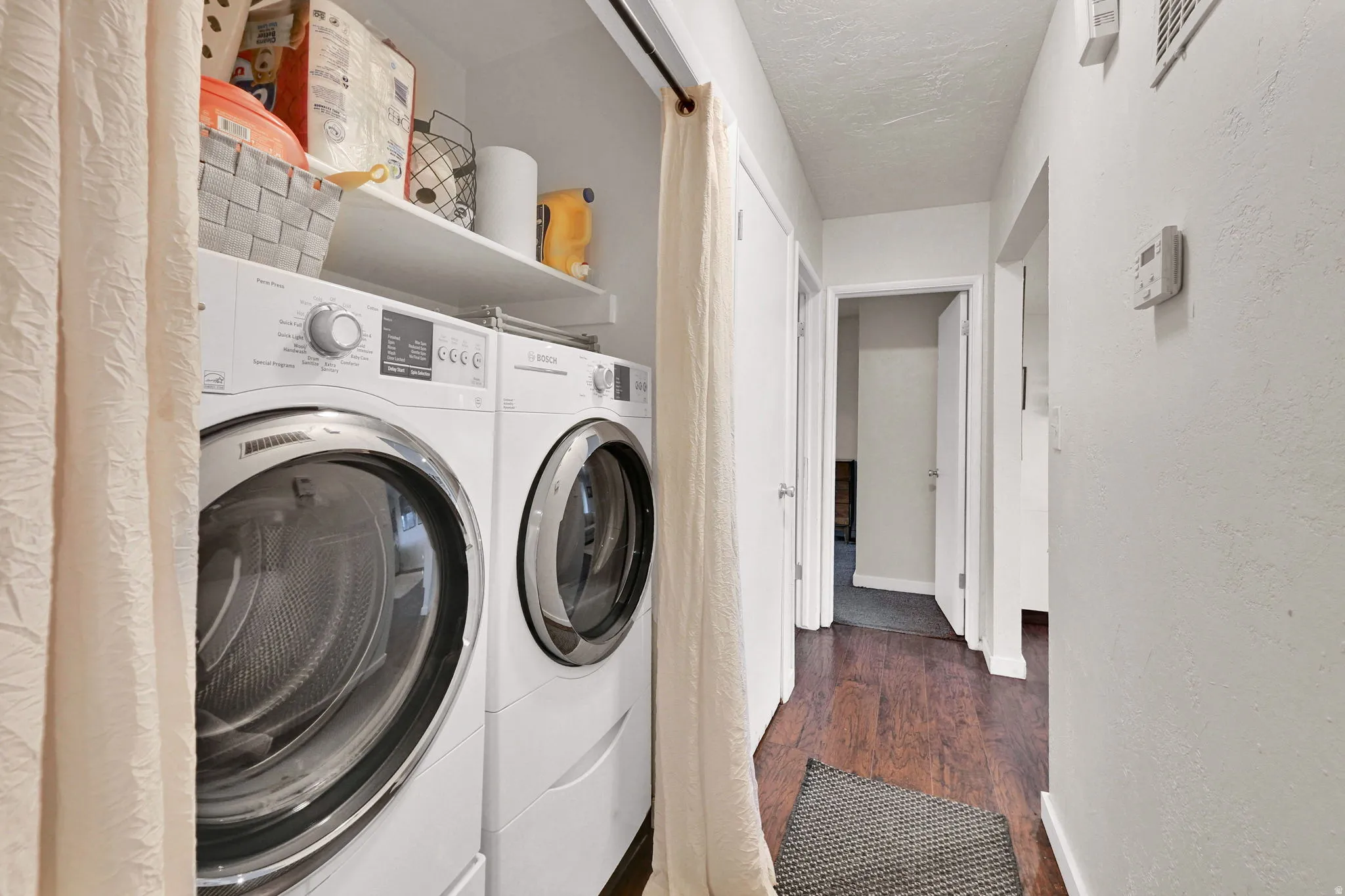 Laundry area featuring dark wood-type flooring, washer and dryer, a textured wall, and a textured ceiling