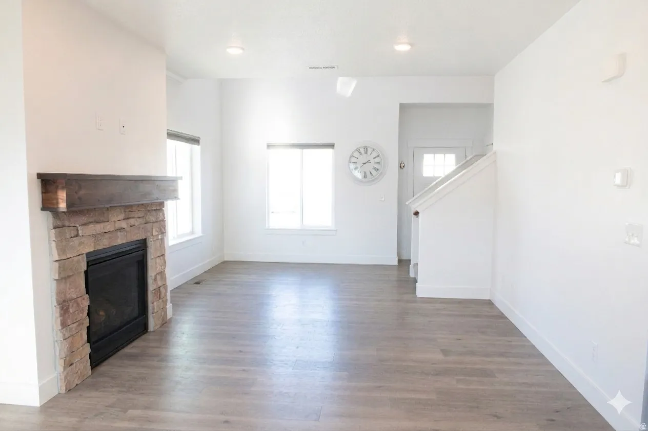 Unfurnished living room featuring wood finished floors and a stone fireplace