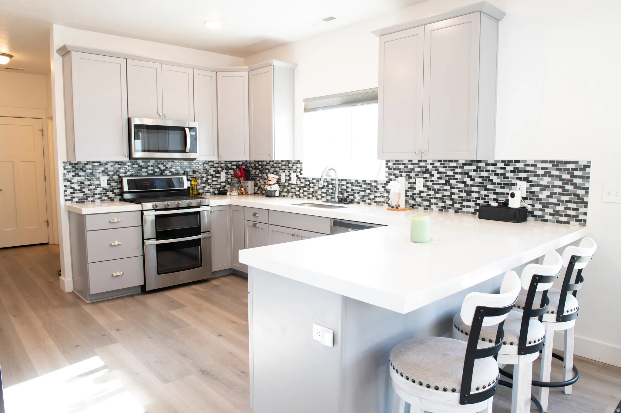 Kitchen featuring a kitchen bar, appliances with stainless steel finishes, a peninsula, gray cabinetry, and light wood laminate  flooring