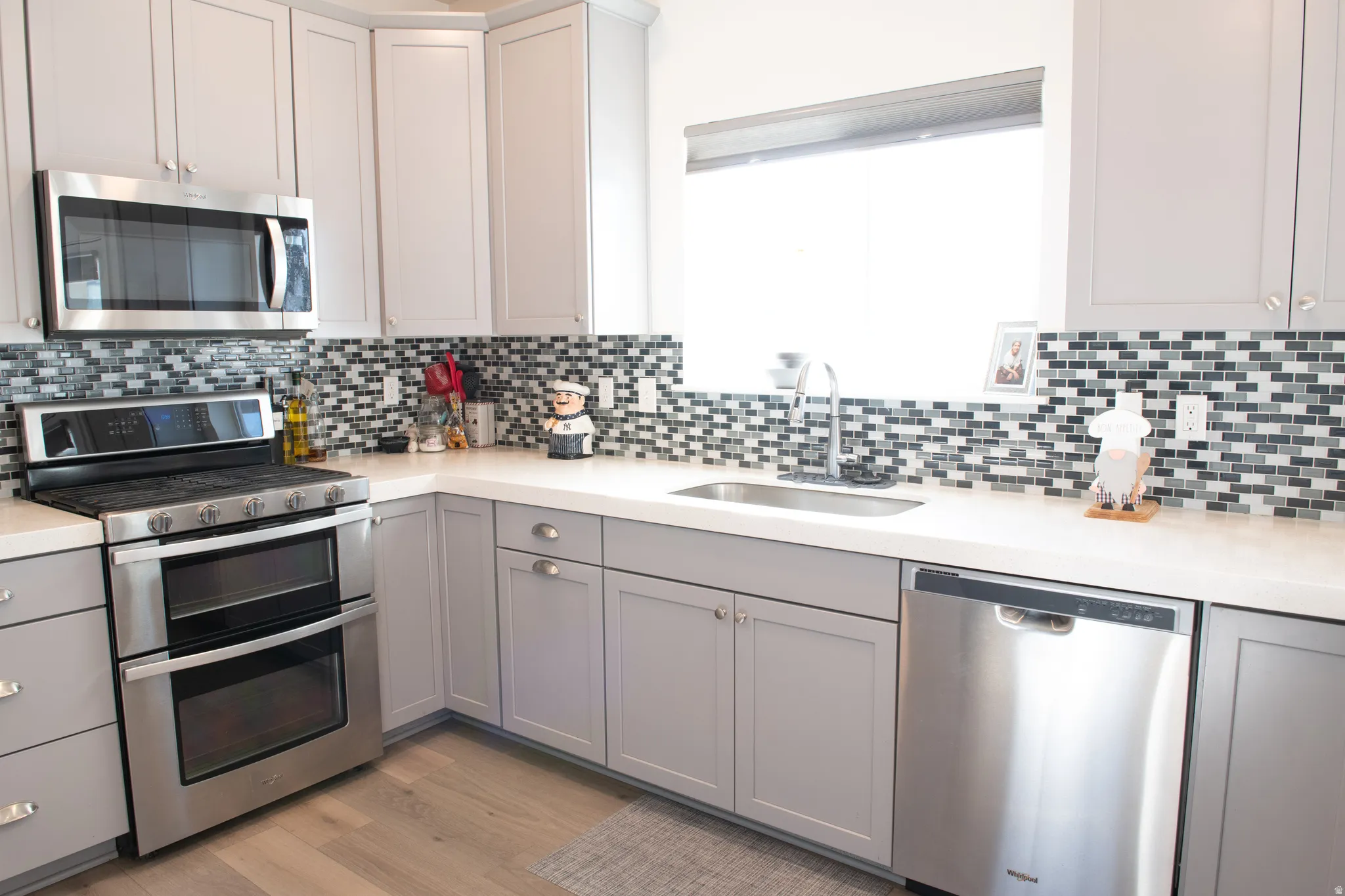 Kitchen featuring gray cabinetry, stainless steel appliances, light wood laminate floors, tasteful backsplash, and light stone countertops