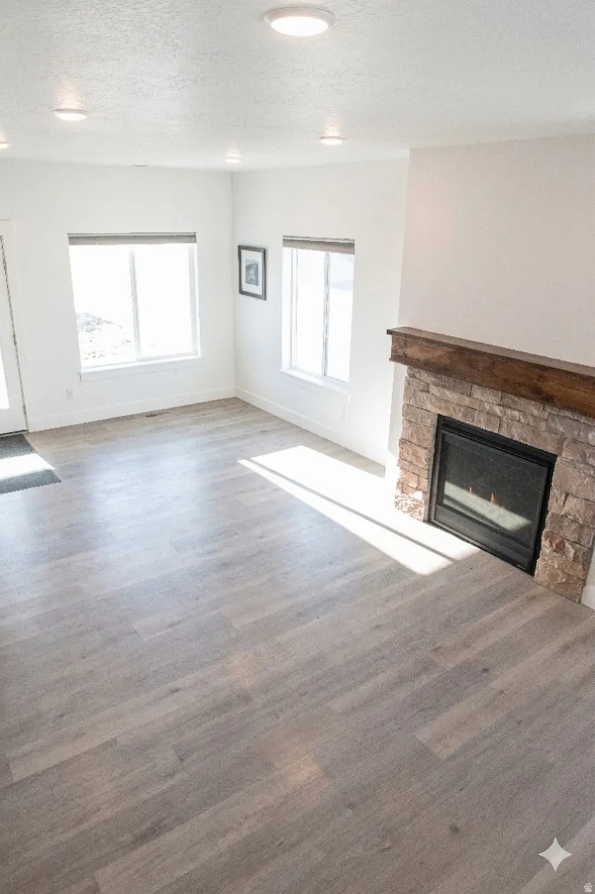 Unfurnished living room featuring a stone fireplace, a textured ceiling, and dark wood-style flooring