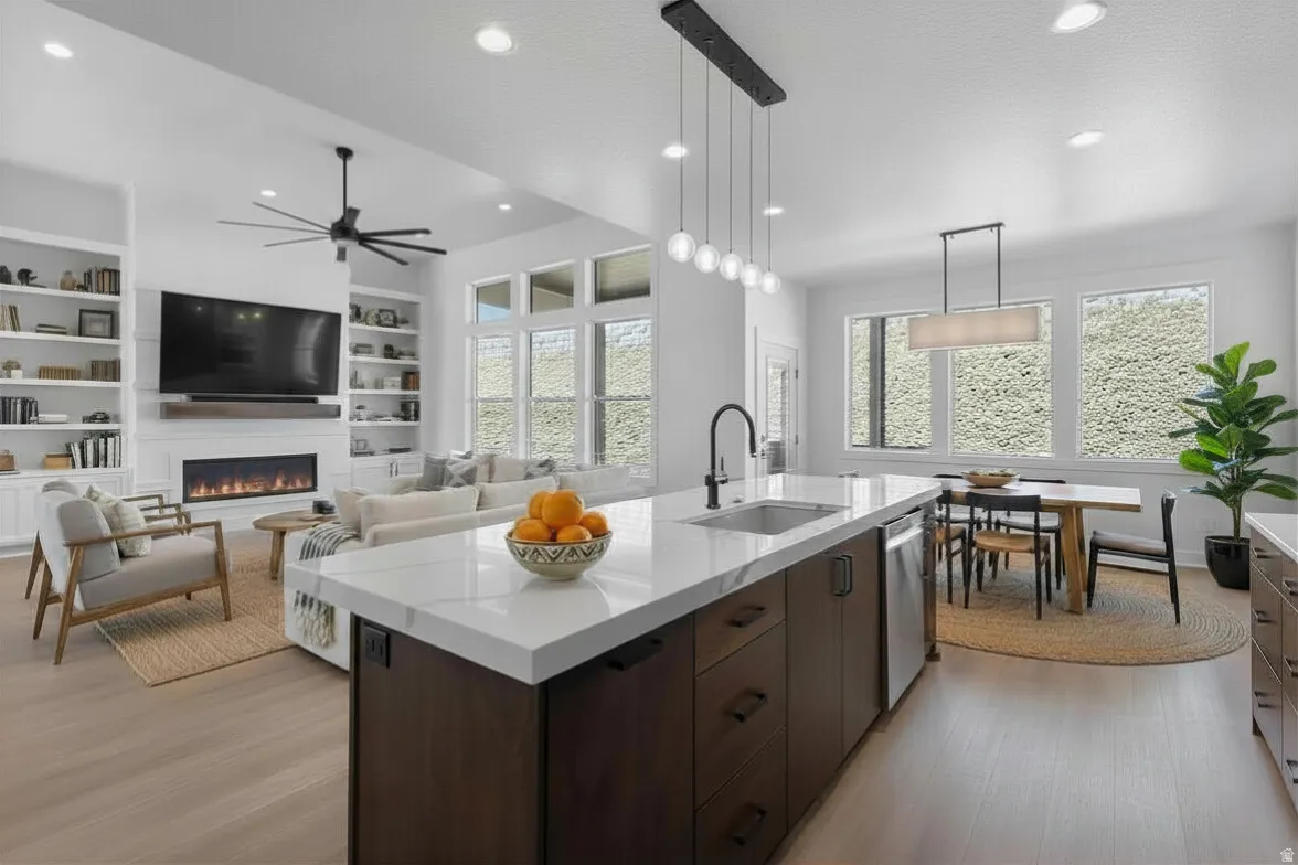 Enhanced staged photo Kitchen featuring dark wood finish cabinetry, decorative light fixtures, an island with sink, a fireplace, and light stone countertops