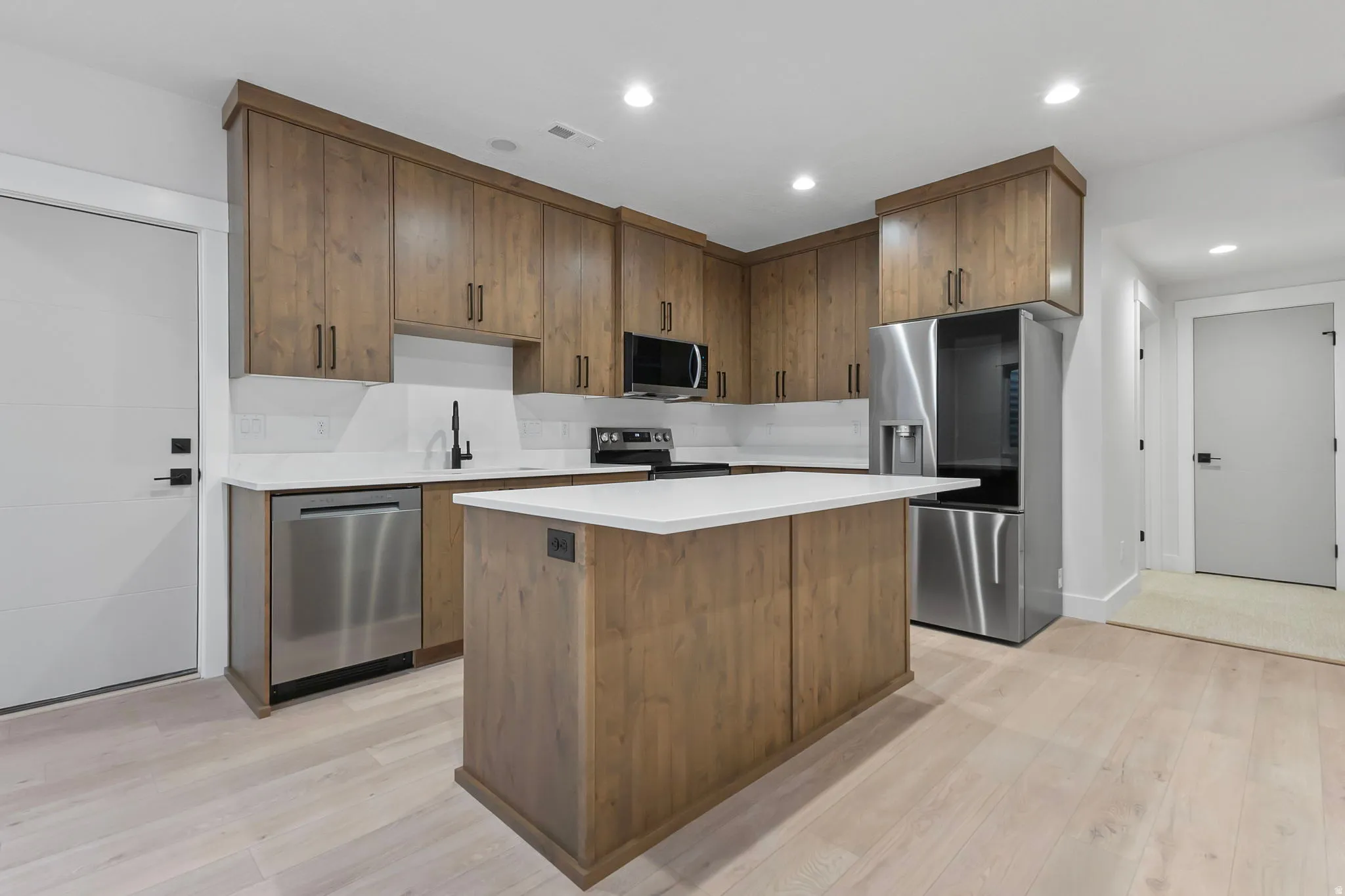 Kitchen featuring wood cabinetry with black hardware, white countertops, stainless steel appliances, and wood-finish flooring