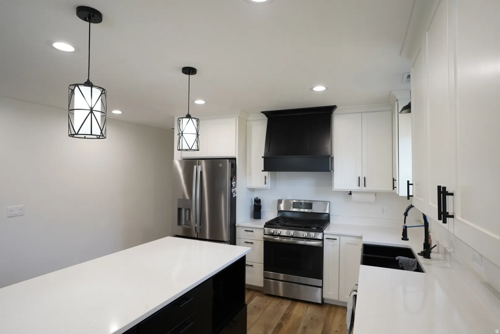 Kitchen with dark cabinets, stainless steel appliances, hanging light fixtures, white cabinetry, and wall chimney range hood